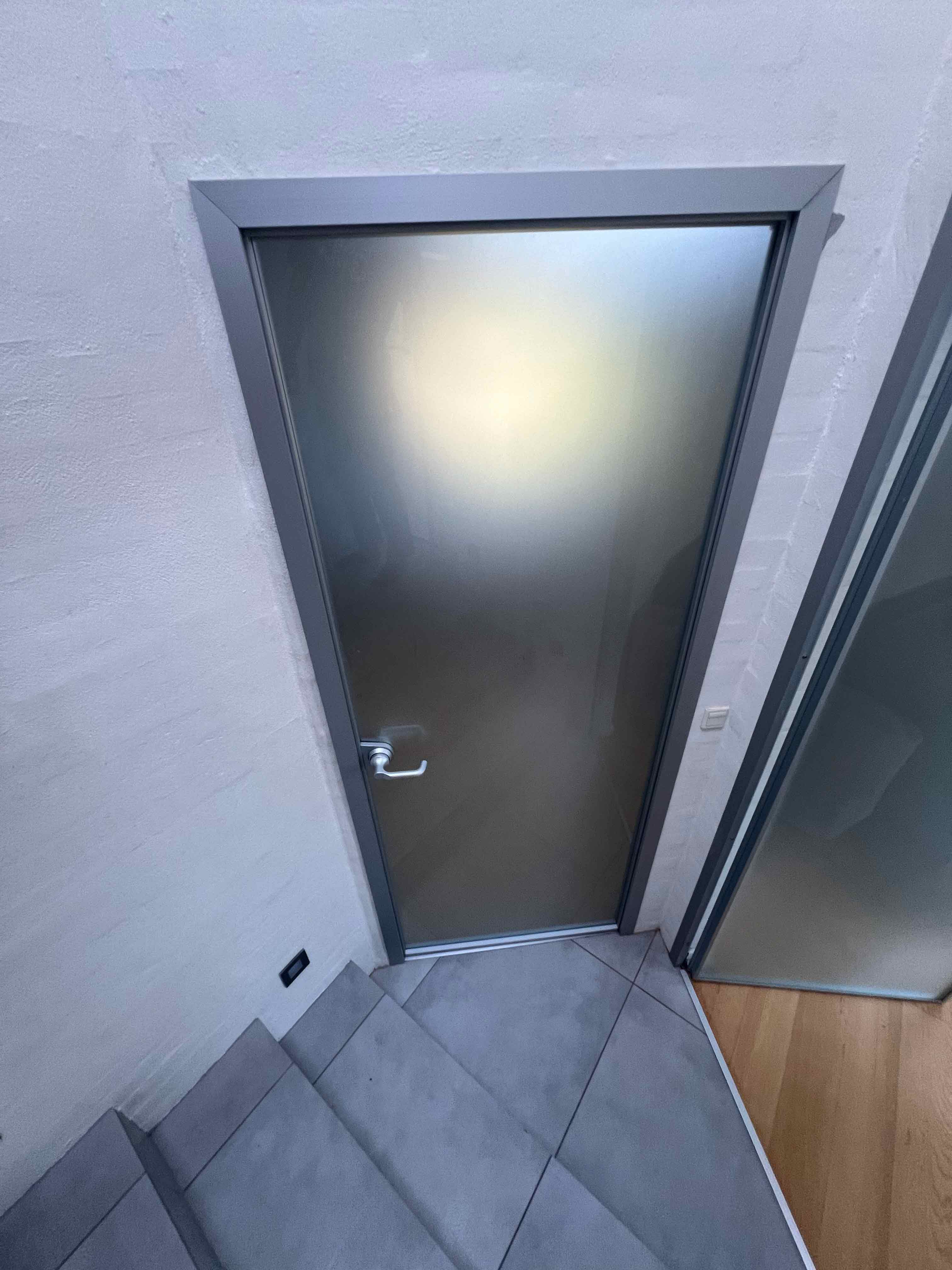 Skræddersyet interiørdør med aluminiumsramme og sandblæst glas, specialbygget af MogaByG for et minimalistisk og stilrent design.